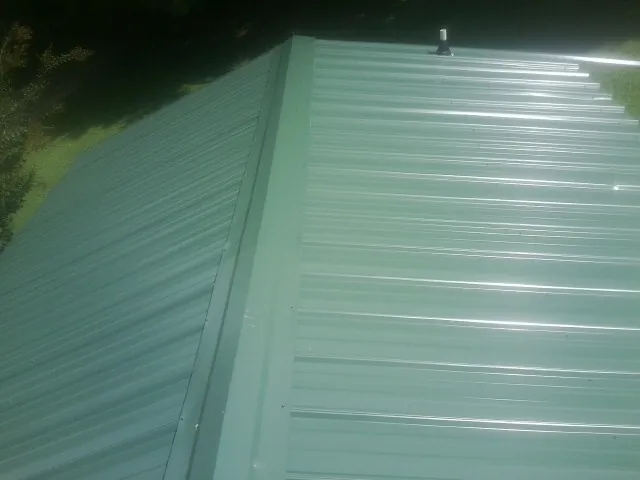New green metal panels meeting at the ridge of a roof — Flat Roof Repair work by our crew in Queen Creek