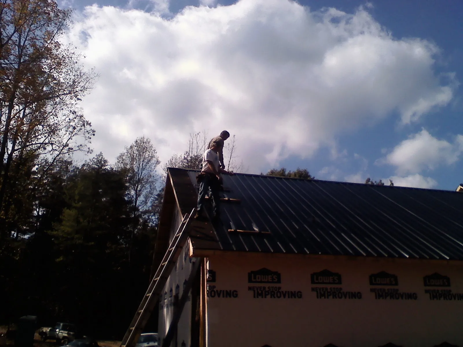 Roofer fastening dark metal panels high against a cloudy sky, from a Roof Inspection job in Queen Creek