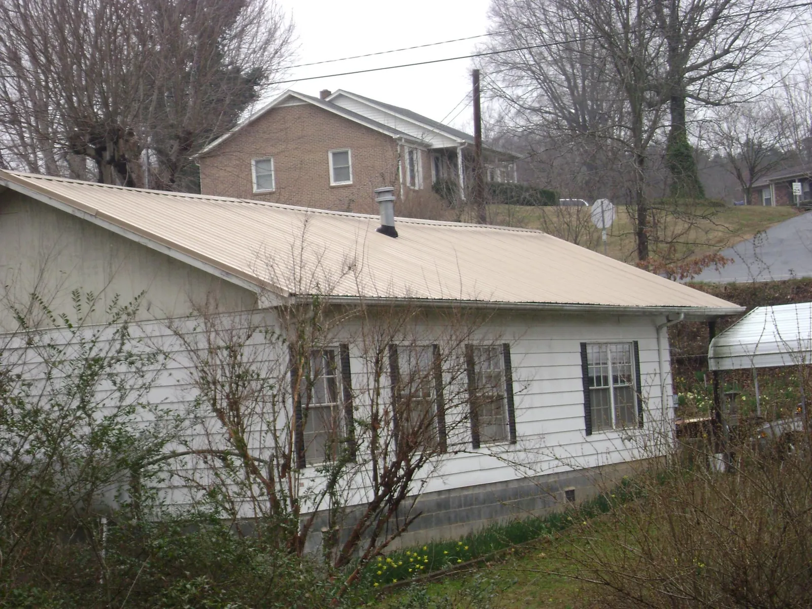 Tan metal roof on a white sided house set into a hillside — Commercial Roofing by Roofing Brothers in Queen Creek